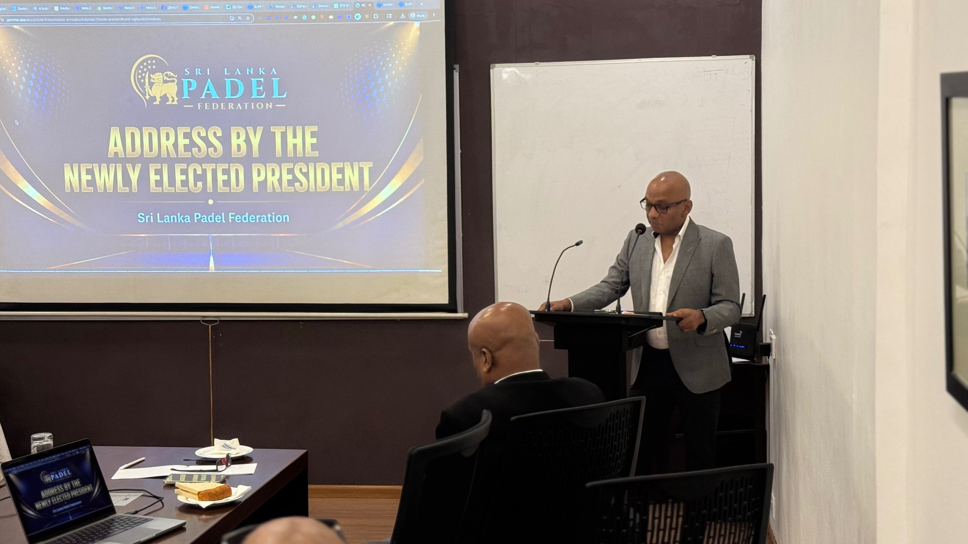 Fazil M. Hussain delivering his address as newly elected President of the Sri Lanka Padel Federation, with the federation slide behind him